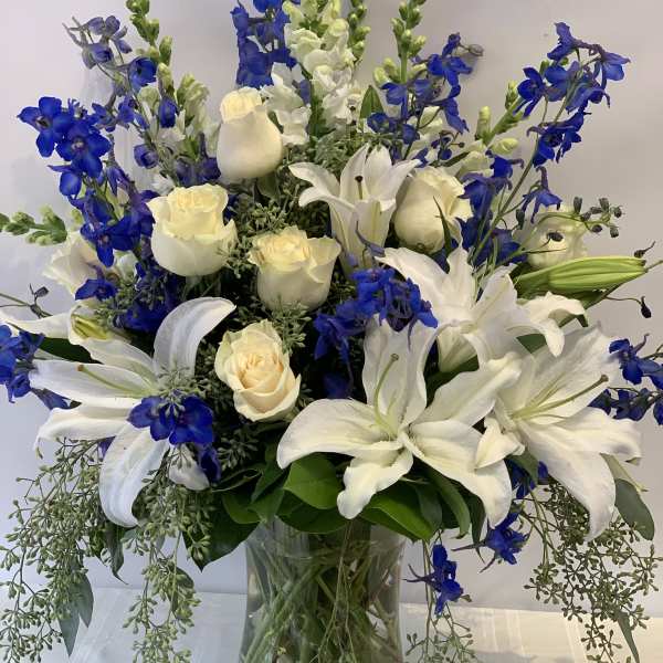 White lilies and cream roses arranged with blue flowers in a glass vase.
