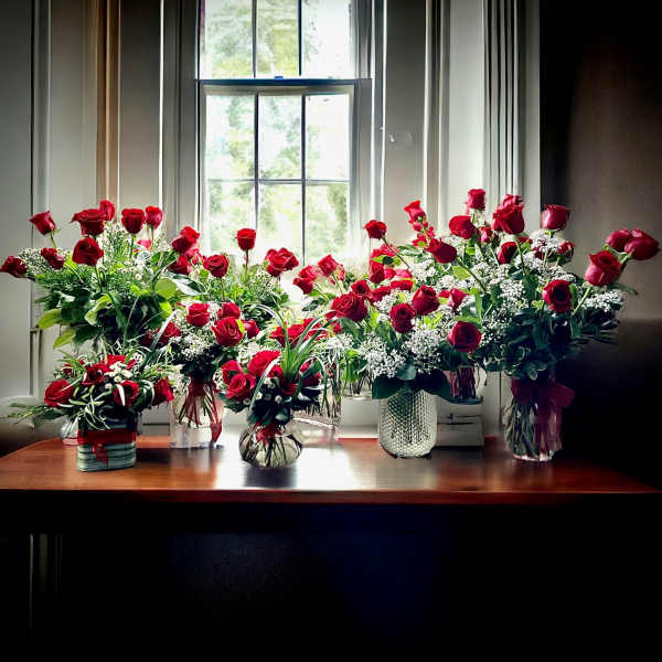 Several red rose arrangements in glass vases on a table