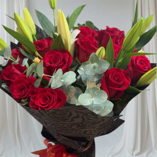 Bouquet of red roses and unopened lilies with eucalyptus in dark wrap