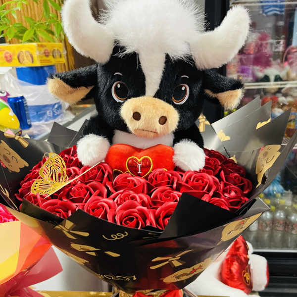 Plush bull sitting in a bouquet of red roses with black wrapping