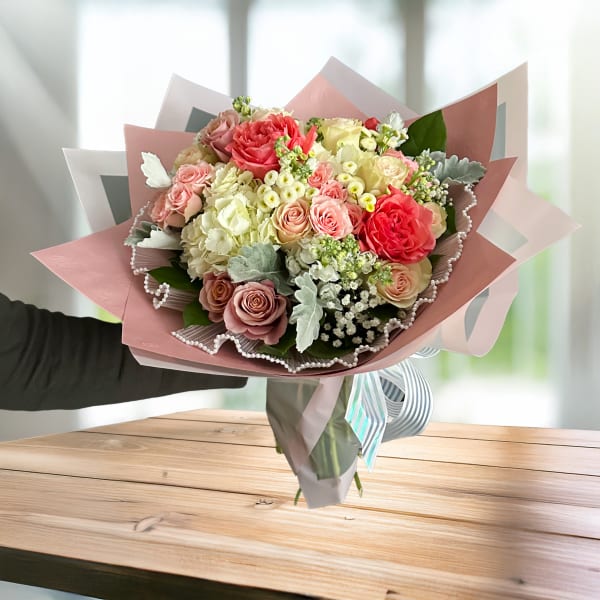 Hand-tied bouquet of pink and cream roses wrapped in pastel paper