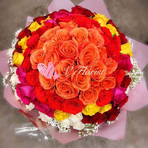 Round bouquet of orange, red, yellow, pink and white roses wrapped in pink paper