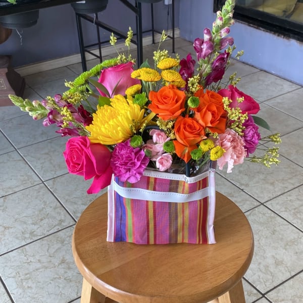 Bright mixed bouquet in a striped gift bag with roses, chrysanthemums, and snapdragons