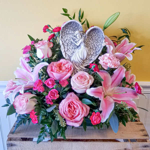 Pink roses and lilies arranged around a heart-shaped angel plaque