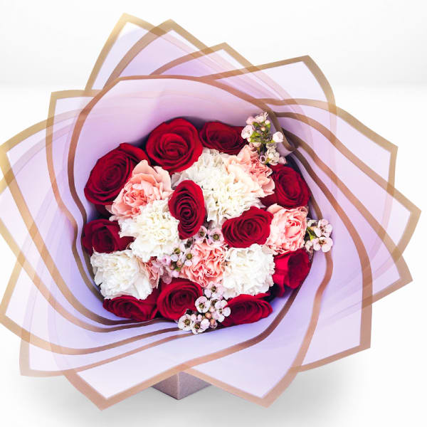 Bouquet of red roses, pink carnations, and white blooms wrapped in lavender paper