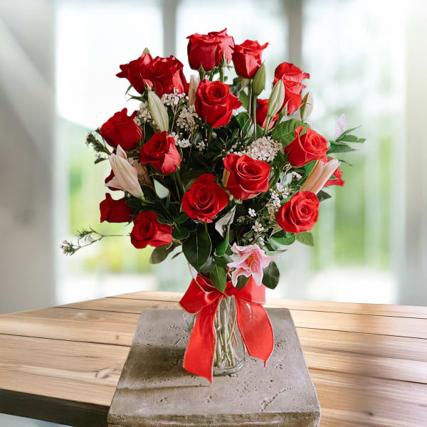 Red roses and white lilies in a glass vase with a red ribbon