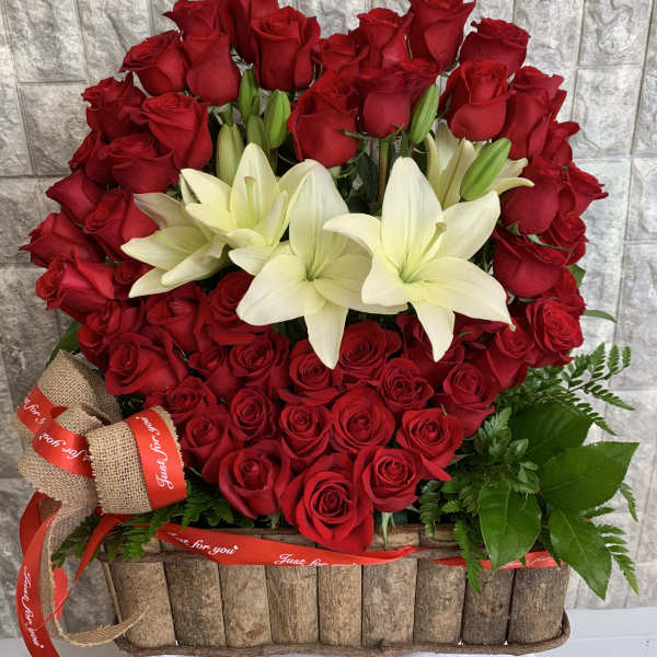 Red roses and white lilies arranged in a rustic basket with ribbon