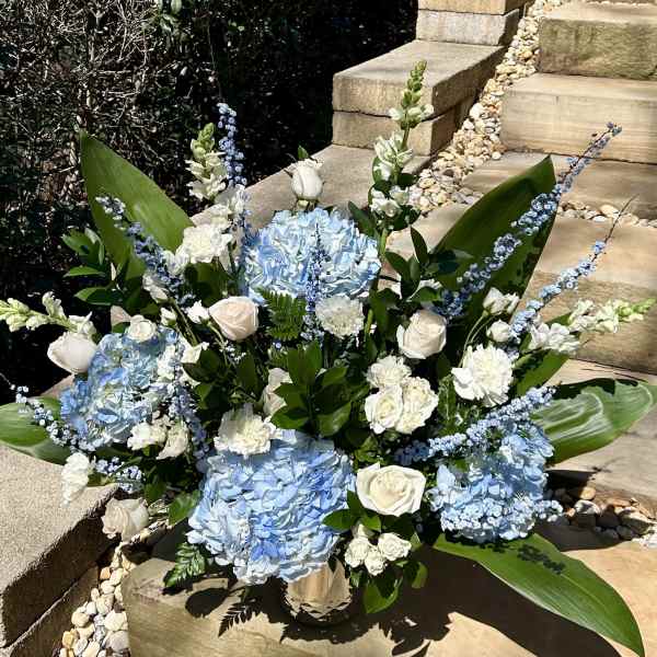 Blue hydrangeas and white roses arranged in a vase with tall blue accents