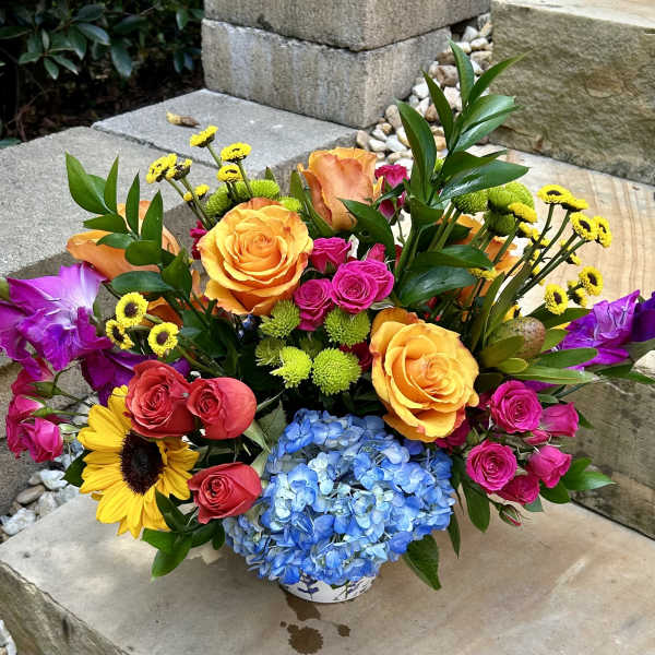 Colorful mixed bouquet in a low white vase with roses, hydrangea, and sunflowers
