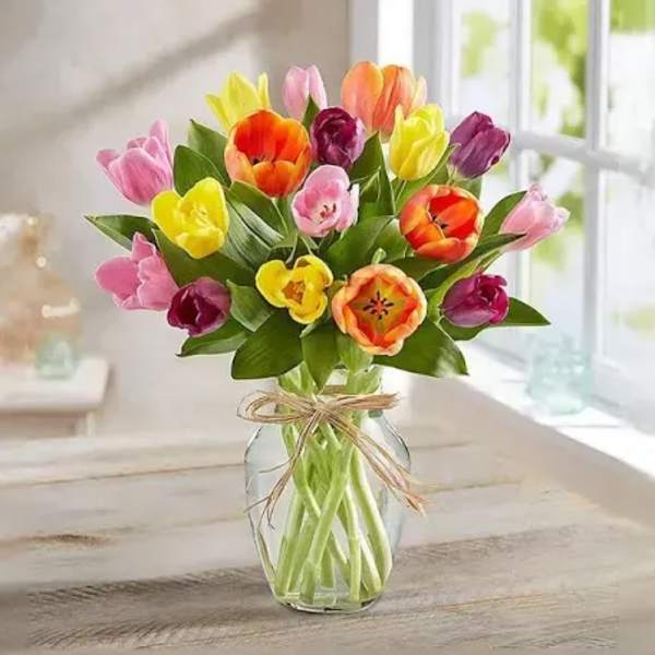 Colorful tulip bouquet in a clear glass vase with a ribbon bow