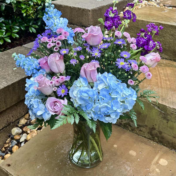 Bouquet of blue hydrangeas, pink roses, and purple flowers in a glass vase