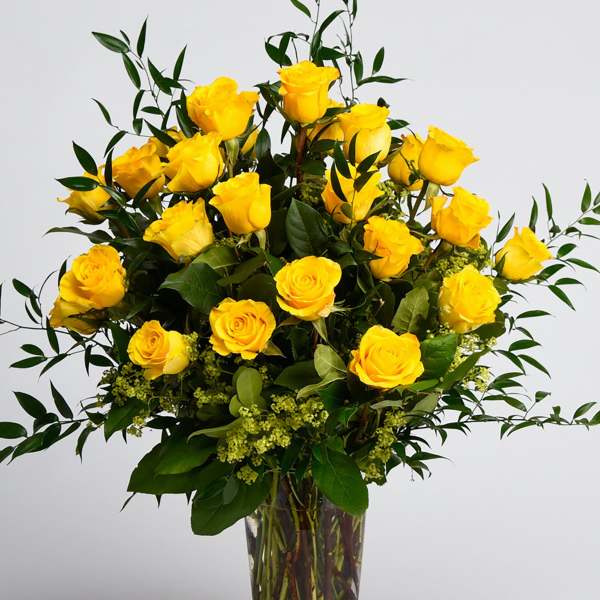 Yellow roses arranged in a clear glass vase with greenery