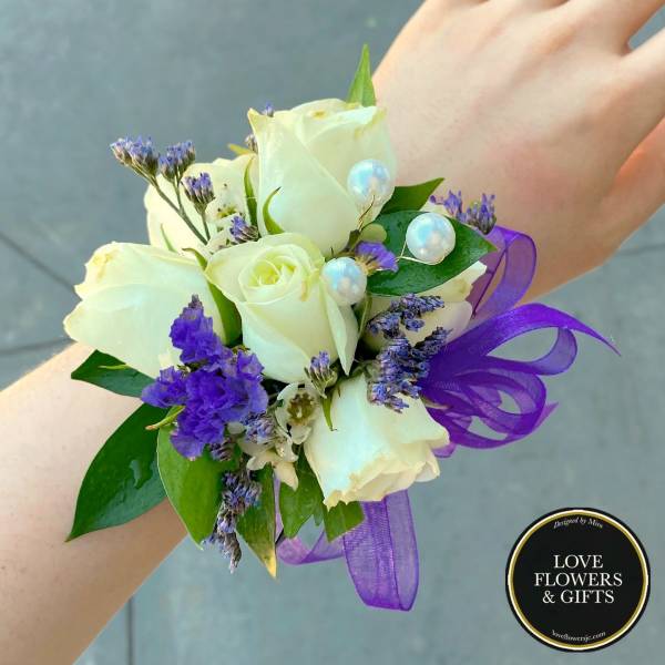 White rose wrist corsage with purple flowers, pearls, and ribbon on a person's arm