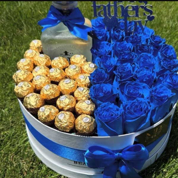 Blue roses and gold-wrapped chocolates arranged in a round gift box with a ribbon.