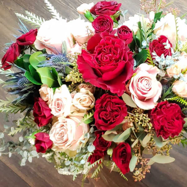 Bouquet of red and blush roses with mixed greenery on a wooden floor