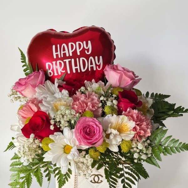 Pink and red flower arrangement with a heart-shaped Happy Birthday balloon in a white bag