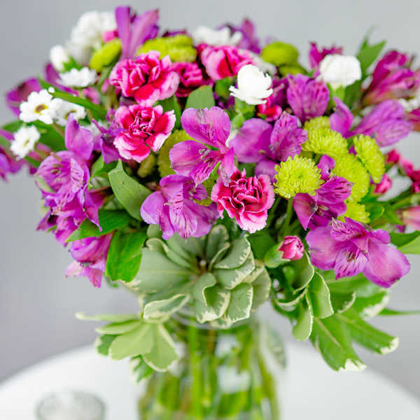 Bouquet of purple alstroemeria, pink carnations, and white daisies in a glass vase