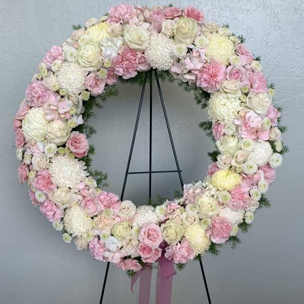 Heart-shaped floral wreath of pink and white flowers on a black stand