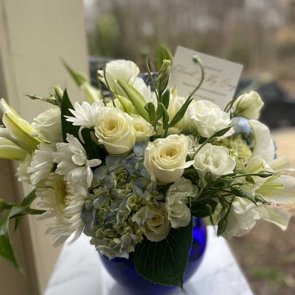 White roses, lilies, daisies, and blue hydrangea in a cobalt vase