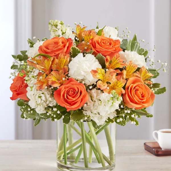 Orange roses and white flowers arranged in a clear glass vase