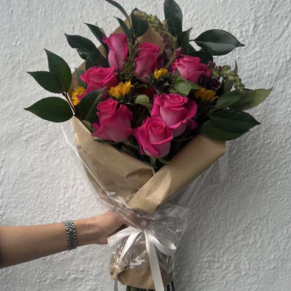 Bouquet of pink roses with small yellow flowers wrapped in brown paper