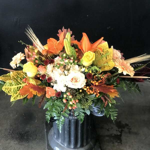 Autumn floral arrangement with roses, lilies, and daisies in a black vase