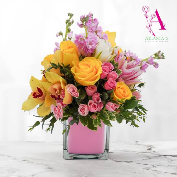 Pink and yellow mixed flower arrangement in a square glass vase