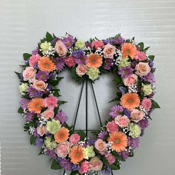 Heart-shaped floral wreath with pink, purple, and orange blooms on a stand