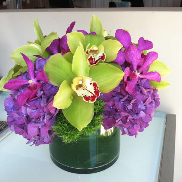 Purple hydrangeas and green orchids in a glass vase