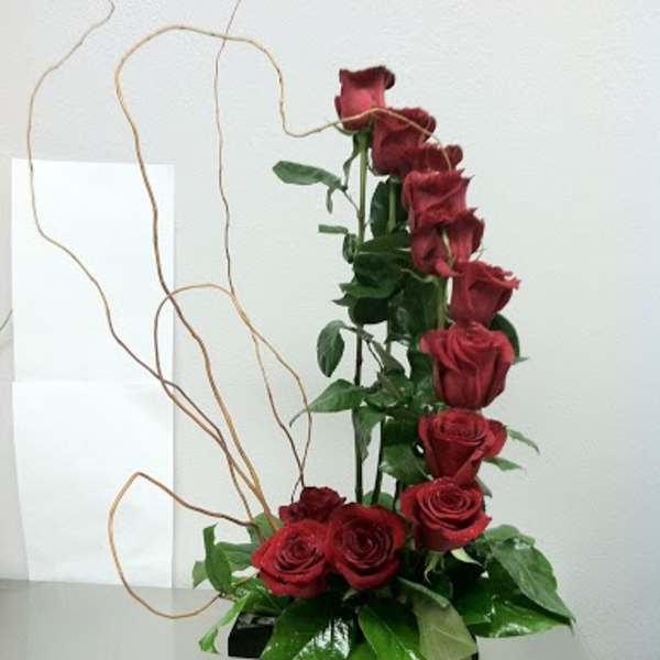 Tall arrangement of red roses in a black box with curly branches
