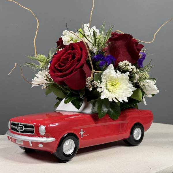 Red roses and white daisies arranged in a red toy car
