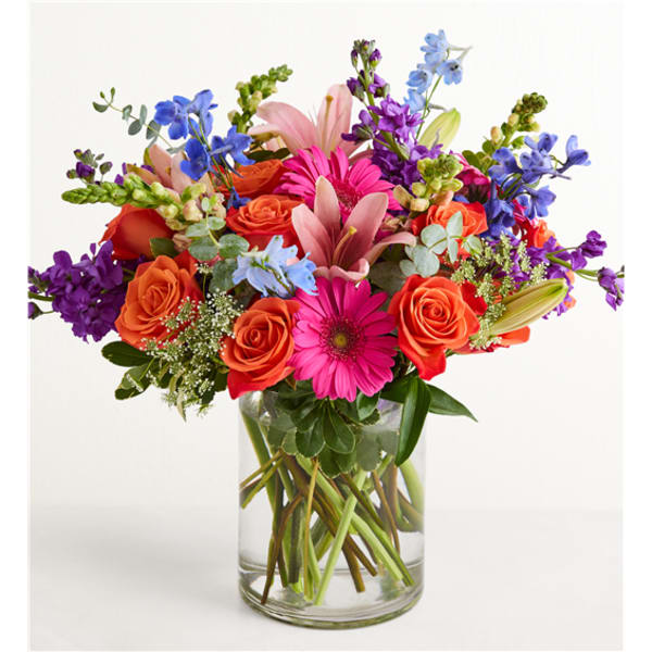 Colorful mixed bouquet in a clear glass vase with roses, lilies, and daisies