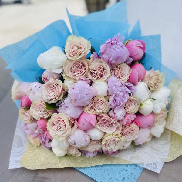 Bouquet of pink and white roses and peonies wrapped in blue paper