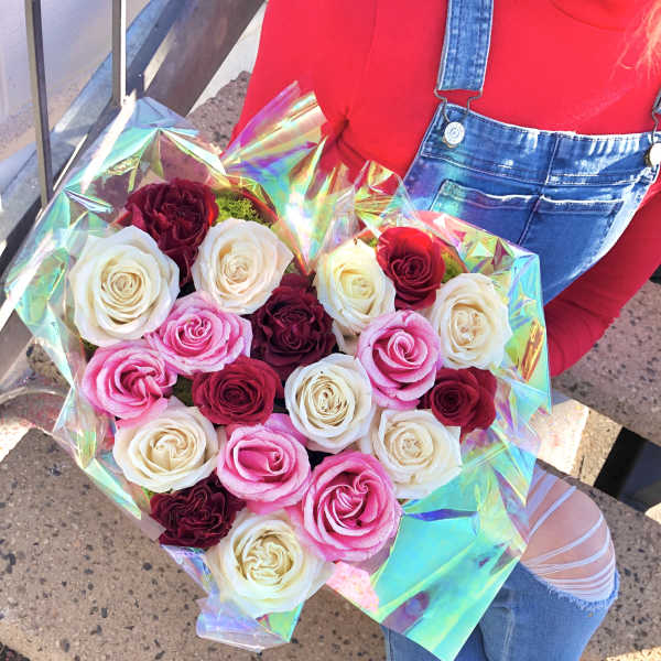 Bouquet of pink, white, and burgundy roses wrapped in iridescent paper