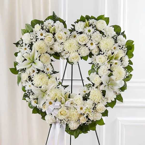 White floral heart wreath on a black stand with a ribbon bow