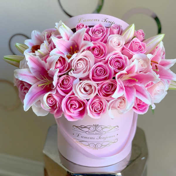Round pink hatbox filled with pink roses and pink lilies on a reflective stand