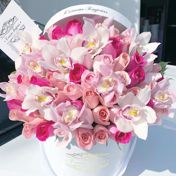 Hatbox arrangement of pink roses and white orchids in a white round box with a card.