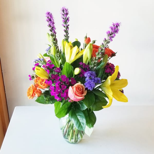 Bouquet of yellow lilies, roses, and purple flowers in a glass vase