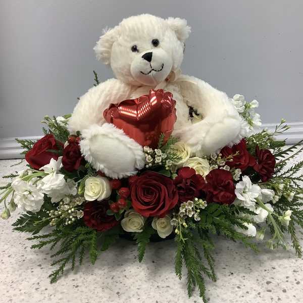 Teddy bear holding a red heart surrounded by red and white flowers