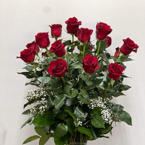 Red roses arranged in a clear glass vase with white filler flowers.