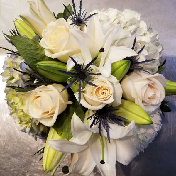 White roses and lilies arranged with pale hydrangea and dark blue thistle