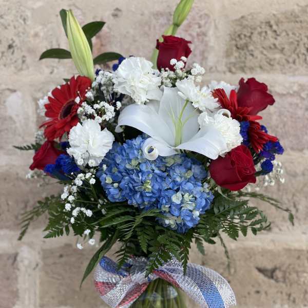 Bouquet of red roses, white lilies, and blue hydrangeas in a glass vase
