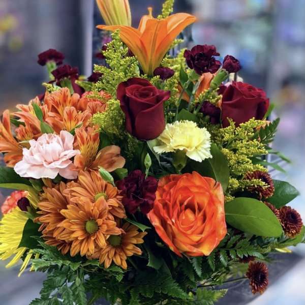 Mixed bouquet of orange, red, and pink flowers in a clear glass vase