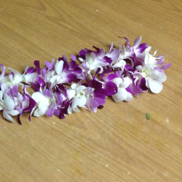 Purple and white orchid lei laid on a wooden surface