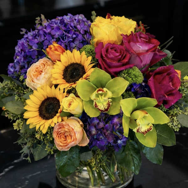 Colorful bouquet with roses, sunflowers, orchids, and hydrangeas in a glass vase