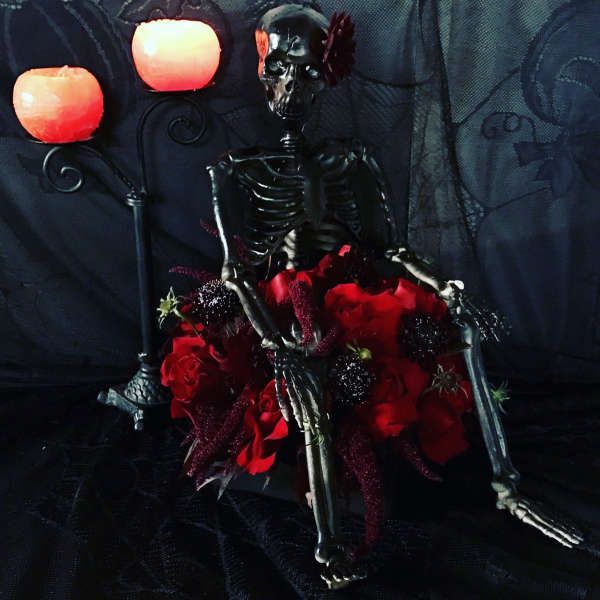 Skeleton figure surrounded by red roses and candles on a dark background