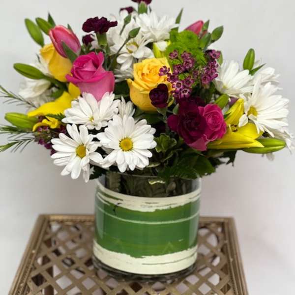 Mixed bouquet of roses, daisies, lilies, and carnations in a glass vase