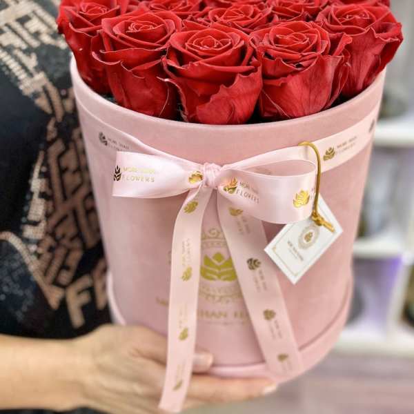 Round box of red roses in a pink hatbox with ribbon and tag