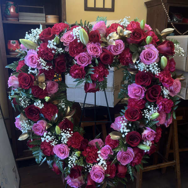 Heart-shaped floral wreath with pink and red roses on a stand