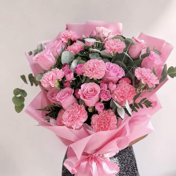 Pink rose and carnation bouquet wrapped in pink paper with a ribbon